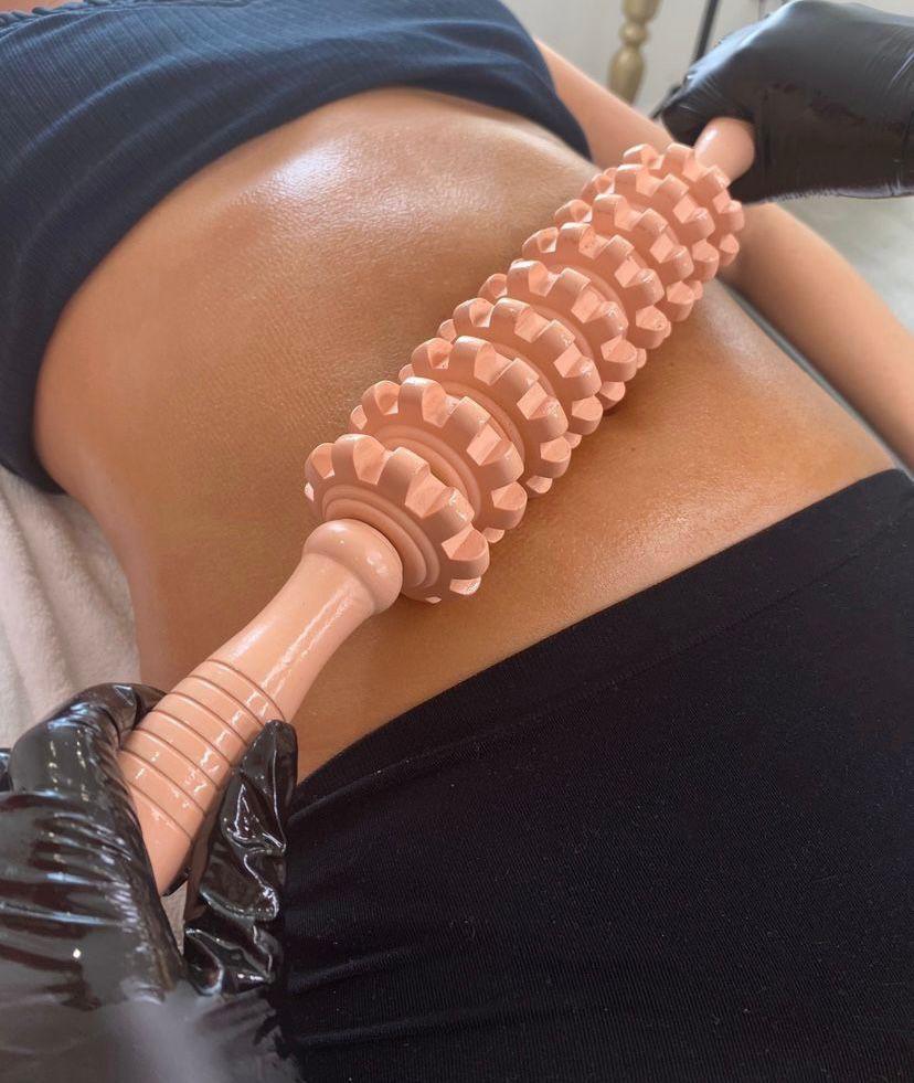 Queenie working a wooden roller across a client's abdomen during Brazilian wood therapy
